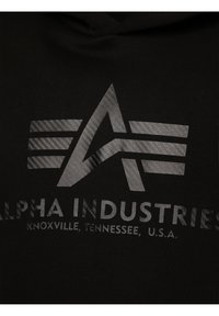 Logo d'Alpha Industries avec un "A" stylisé et trois bandes horizontales au-dessus du texte indiquant "Knoxville, Tennessee, États-Unis" sur tissu noir.