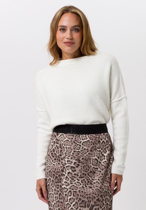 Weißer, flauschiger Pullover mit Rundhalsausschnitt, kombiniert mit einem Leopardenmuster-Rock mit schwarzem Bund. Weiche Textur, lockere Passform und auffälliges Muster.