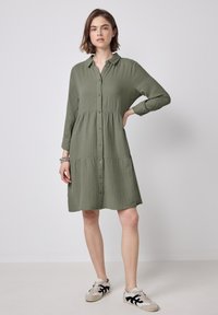 Vestito verde con colletto, design a strati, maniche lunghe e tessuto texturizzato. Abbinato a sneaker casual.