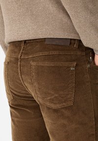 Pantaloni in velluto a coste marrone con righe verticali, dotati di tasche posteriori classiche e una toppa in pelle sulla vita.