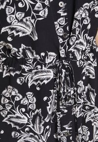 Robe en tissu noir avec un motif floral blanc, dotée de boutons et d'une ceinture ajustable pour un meilleur ajustement. Texture douce avec un design décontracté.