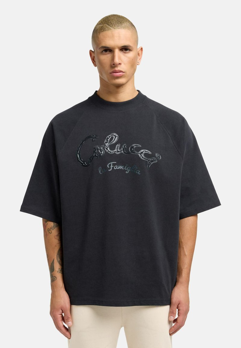 Zwarte oversized T-shirt met korte raglanmouwen, voorzien van een glanzend, geborduurd logo op de borst. Makkelijk katoen textuur.