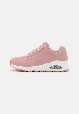 Zapatilla deportiva de color rosa claro con un upper sintético texturizado, entresuela blanca, suela de goma y detalles perforados en los laterales.