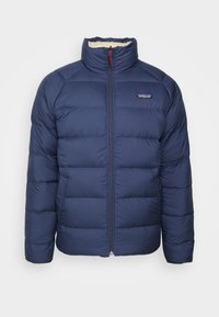 Veste matelassée bleu marine avec fermeture éclair sur le devant, col haut et design matelassé. Comprend une doublure en polaire et un petit logo sur la poitrine.