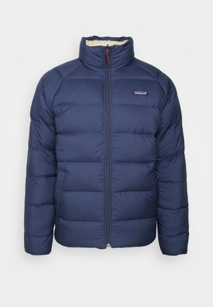 Veste matelassée bleu marine avec fermeture éclair sur le devant, col haut et design matelassé. Comprend une doublure en polaire et un petit logo sur la poitrine.