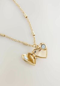 Goldener herzförmiger Anhänger mit Scharnier, geöffnet um das leere Innere zu zeigen, an einer goldenen Kette mit zylindrischen Gliedern.