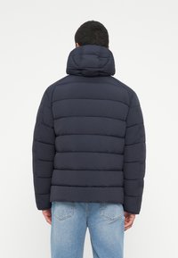 Granatowa puchowa kurtka z wysokim kołnierzem, pikowanym wzorem i gładką teksturą. Posiada elastyczne mankiety i krótki krój, idealna do noszenia na co dzień.