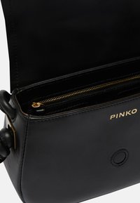 Borsa a tracolla in pelle nera con una cerniera e accessori dorati. Presenta una superficie liscia, un logo ricamato e un dettaglio arrotondato sul lato.