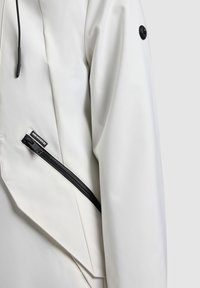 Bijela rukav jakne s crnim džepom na patentni zatvarač i crnim vezicama, s detaljnim šavovima i malom oznakom marke blizu patentnog zatvarača.