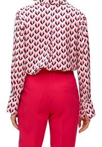 Blusa a maniche lunghe in rosa e bianco con motivo a zigzag, abbinata a pantaloni su misura di un vivace rosa. Tessuto liscio e design aderente.