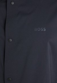 Fekete dzseki sima szövettextúrával, gombzárral és diszkrét, dombornyomott "BOSS" logóval az elülső bal oldalon.