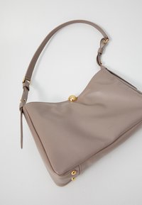 Light beige leather handbag with a curved shape, gold hardware accents, adjustable shoulder strap, and a smooth texture.