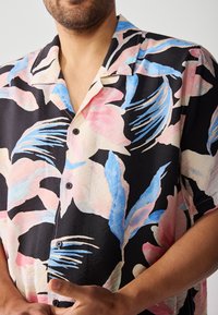 Short-sleeve button-up shirt featuring a black base with large pink and blue floral patterns, textured fabric, and a relaxed fit.
