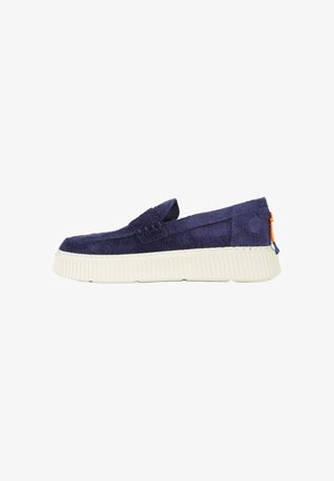 Mocassino slip-on in suede blu navy con suola spessa bianca zigrinata e piccolo tirante arancione e blu sul tallone.
