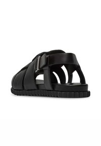 Sandalias de cuero negro con un diseño abierto, múltiples correas y un detalle de hebilla, sobre una suela de goma negra texturizada.