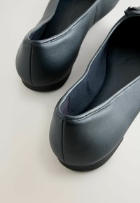 Schwarze Lederflats mit einer glatten Textur, abgerundeter Spitze und niedrigem Absatz. Das Innere ist mit einem dunklen Stofffutter ausgestattet. Nahtdetails sind sichtbar.