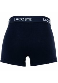 Tengerész-kék pamut boxeralsó fehér Lacoste logóval a derékpánélon, szoros illeszkedéssel és közepes magasságú kialakítással.