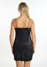 Robe mini noire avec une finition texturée et brillante. Dotée de fines bretelles en chaîne et d'un ourlet droit sur le bas.