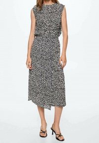 Černobíle vzorované midi šaty s krátkými rukávy, nabíraným pasem a splývavou siluetou, doplněné o černé sandály na pásky.
