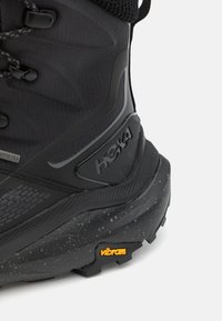 Svart vandrarsko med en texturerad ovandel, Gore-Tex-material och en Vibram-sula med ett flammigt mönster. Logotypen visas på sidan.