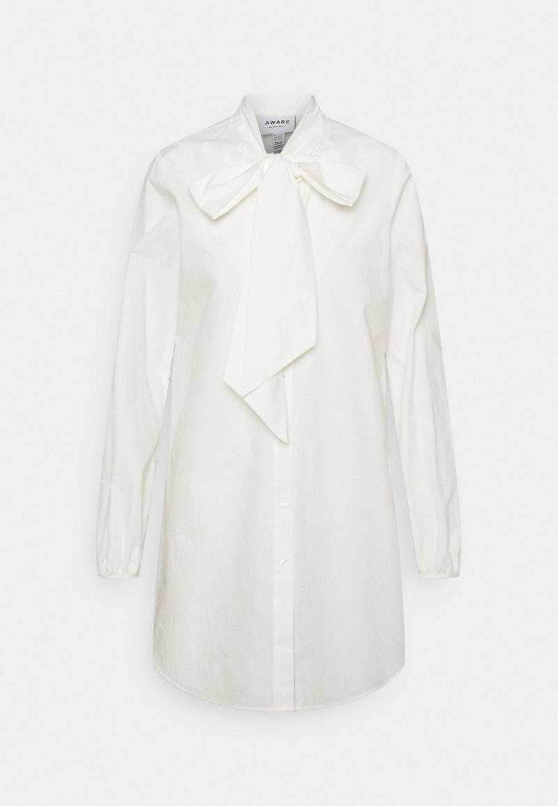Longue blouse blanche boutonnée à manches longues avec un grand nœud décoratif noué au col.