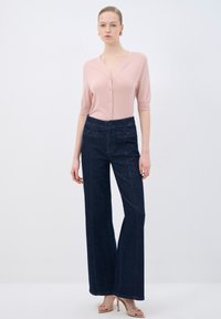 Cardigan de manga corta color rosa claro con botones, combinado con jeans de pierna ancha azul oscuro, con cintura alta y bolsillos frontales.