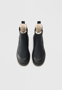 Zwarte leren enkelboots met een zachte beige bontvoering, trekbandjes aan de achterkant en een dikke rubberen zool. Gladde textuur met een ronde neus.