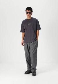 Mørkegrå oversized t-skjorte med en liten logo, kombinert med løse grå bukser og svarte klumpete sneakers. Solbriller fullfører antrekket.