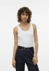 Witte katoenen tanktop met brede schouderbanden, gecombineerd met donkere denim high-waisted jeans en een zwarte riem met een zilveren gesp.