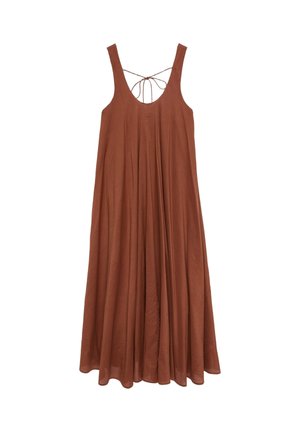 Kobieta w bezrękawowej, rdzawoczerwonej sukience maxi z odkrytymi plecami i wiązaniem z tyłu, idąca w czarnych butach z odkrytą piętą na szarym tle.