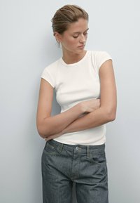 Witte short-sleeve t-shirt met een ronde halslijn, gedragen met donkerdenim jeans met lichte stiksel en een knoopsluiting.