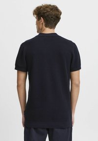 Navy blue, short-sleeved polo shirt; textured fabric with a slim fit; folded sleeves; collar at the neckline; discreet brand label on the side.