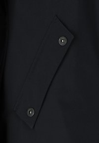 Navy blue raincoat fabric with a smooth texture, featuring a tab with a black snap button. The design includes a clean, minimalist cut.