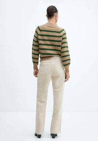 Maglione lavorato a maglia marrone con strisce verdi, design corto e maniche lunghe. Abbinato a pantaloni a zampa d'elefante beige chiaro e tacchi neri.