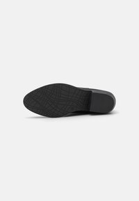 Suela de zapato de goma negra con un patrón texturizado; punta ancha y redondeada con un tacón sutil; diseño simple y funcional.