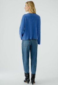 Blauwe fuzzy trui met een losse pasvorm, gecombineerd met hooggetailleerde, lichtblauwe denim jeans. Zwarte haklaarzen maken de outfit af.