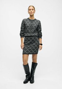 Ensemble en tricot gris composé d'un pull et d'une jupe avec un motif en losanges, comprenant des boutons, des poignets côtelés et des bottes en cuir noir jusqu'au genou.