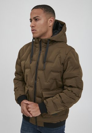 Braune Pufferjacke mit Kapuze, ausgestattet mit einem Reißverschluss, gerippten Bündchen und Fronttaschen. Strukturiertes, gestepptes Design mit matter Oberfläche.