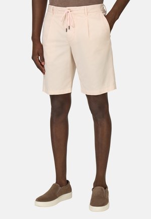 Pantalones cortos de color rosa claro con cintura ajustable, pliegues y bolsillos laterales, combinados con zapatos marrones sin cordones y una blusa ajustada. Textura de algodón suave.
