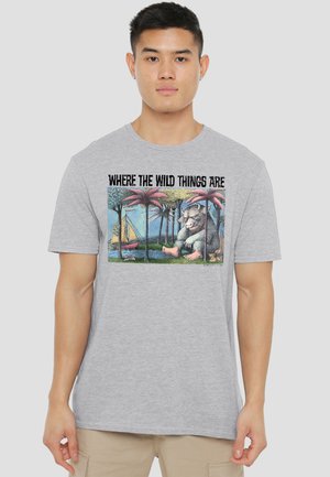Young man wearing a gray T-shirt with a "Where the Wild Things Are" forest and monster illustration and a sailboat.
