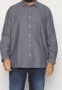 Camicia button-up blu navy con un motivo geometrico, maniche lunghe e colletto. Presenta una vestibilità rilassata e bottoni bianchi sul davanti.