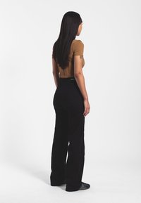 Top corto ajustado marrón de manga corta combinado con jeans negros de tiro alto y acampanados. La modelo se encuentra de espaldas a la cámara, mostrando la forma del atuendo.