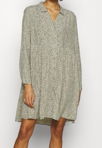 Vestido de manga corta en tejido ligero, con un diseño estampado en verde y negro, cuello, frente abotonado y silueta acampanada.