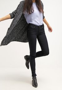 Jeans skinny neri abbinati a una maglietta azzurro chiaro e a un lungo cardigan grigio texturizzato. L'outfit è completato da eleganti stivaletti neri alla caviglia.