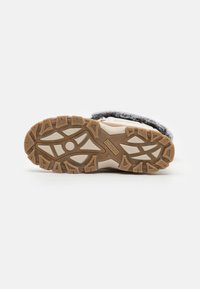 Suela de un zapato con una superficie de goma marrón texturizada y surcos profundos, diseñada para ofrecer tracción, y una entresuela de color claro.