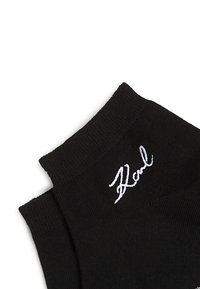 Calcetines de algodón negros con una textura acanalada y una firma bordada blanca en el puño. El diseño es simple y minimalista.