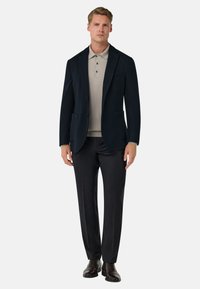 Námořnický blazer se dvěma předními kapsami přes světle béžové polo tričko, doplněný tmavými kalhotami a hnědými koženými botami. Čistý design, na míru padnoucí střih.