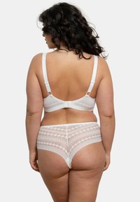 Ensemble de lingerie en dentelle blanche comprenant un soutien-gorge et un slip assorti, mettant en valeur des motifs géométriques complexes, des bretelles réglables et des bordures en forme de vagues, présenté de dos.