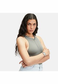 Grå ribbad bralette med hög halsringning. Modellen bär silverkedjesmycken och jeansshorts. Bakgrunden är helt vit.