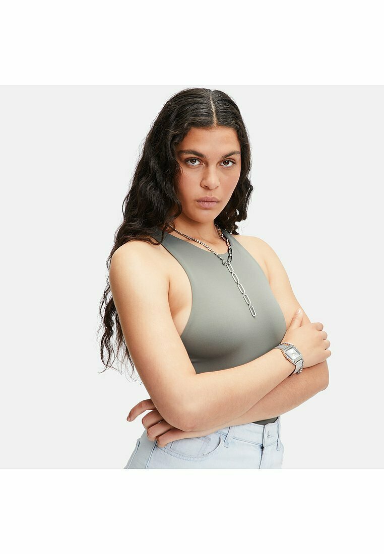 Grå ribbad bralette med hög halsringning. Modellen bär silverkedjesmycken och jeansshorts. Bakgrunden är helt vit.